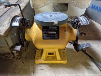 Front view of ProMart bench grinder showing grinding wheel, tool rests, safety guards, and motor housing.