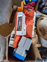 Box with various vintage Hot Wheels race track parts including orange track sections and white and blue plastic parts