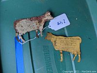 Two vintage metal advertising cows with De Laval Cream Separator details, showing rust and wear, laid on a green container surface.