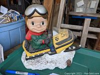 Side view showing child in green outfit and yellow snowmobile on snow base