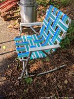 Full view of the folding lawn rocking chair showing blue, green, and white webbed fabric on a metal frame with rocking base outdoors.