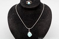 Full view of silver necklace with teardrop Larimar stone pendant and matching Larimar ring on black velvet display.