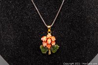 Front view of coral and jade floral gold-tone pendant on silver chain displayed on black velvet background