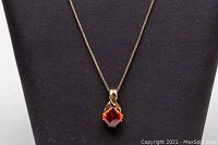 Front view of necklace and pendant displayed on black mannequin showing the orange gemstone pendant.