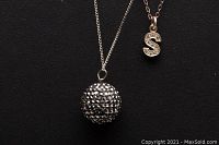 Close-up image showing the pavé ball pendant and the letter S pendant with small stones on silver chains.