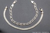 Two sterling silver bracelets against a dark background, showing the mesh and link chain styles with clasps open.