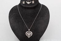 Full view of necklace with heart-shaped filigree pendant, ring and earrings displayed on black velvet stand
