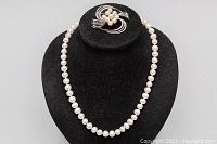 Full view of the pearl necklace with brooch on black display stand.