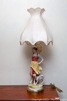 Full view of the hand painted European porcelain figural table lamp, showing the figurine, shade, and brass base.