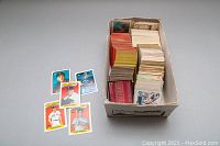Photo showing a shoebox packed with assorted baseball cards with some cards displayed next to the box revealing vintage player portraits.