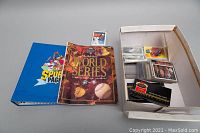 Overview of the lot including the blue sports card album, the 1993 World Series souvenir scorebook, and a white box containing numerous baseball cards