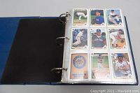 Open binder showing plastic pages with assorted baseball cards featuring players in various poses and team uniforms.