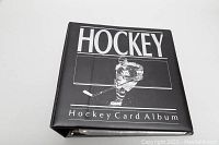Closed black hockey card album binder with 'HOCKEY Hockey Card Album' text on the cover and a player image.