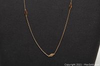 Close-up of necklace chain showing fine links and small elongated hexagonal decorative elements on a black display.