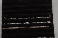 Top view showing all three silver bracelets laid side by side on black fabric background, displaying chain styles and clasps.