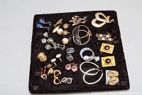 Top view of all 22 assorted costume earrings displayed on a black velvet surface showing variety of designs and materials.