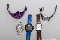 Five men's wrist watches arranged flat on a white surface, showing all watches from a top-down angle.