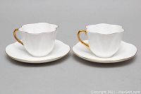Two Shelley white scalloped teacups with gold gilt trim and matching saucers shown from the front and side.