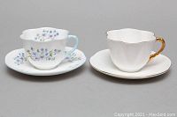 Two Shelley teacup and saucer sets side by side, showing blue floral and gold gilt designs
