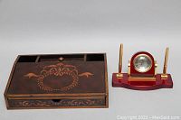 Red and gold-tone quartz desk clock with twin pen holders and matching pens next to the wooden desk organizer with decorative inlay.