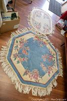 Photo showing two rugs on wooden floor, an octagonal blue floral wool rug in front and oval cream floral wool rug in back