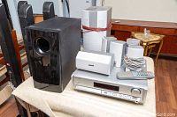 Photo showing Panasonic subwoofer, multiple white speakers, DVD receiver unit, and remote control on table.