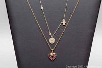 Two layered silver-tone necklaces displayed on a black backdrop, showing distinct pendants and chain styles.