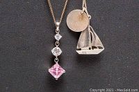 Close-up image of two 925 silver necklaces with pendants: one sailboat with round disc and one multi-stone pink and clear pendant.