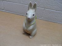 Front view of white ceramic rabbit figurine with painted eyes, nose and green collar
