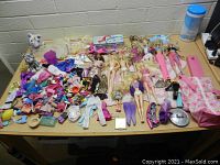 Wide view of large assortment of Barbie dolls, doll clothes, shoes, accessories, and other small toys laid out on a table.