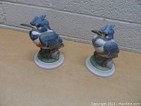 Two blue and white porcelain kingfisher bird figurines on oval bases with branch and grass details, about 5 inches each.