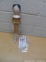 Full view of wooden peg doll standing on a surface next to a laminated informational sheet.