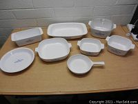 Eight vintage Corning Ware dishes with blue Cornflower pattern on a wooden table against a gray block wall.