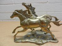 Front view of the brass statue showing two horses running with detailed manes and muscular bodies on a base.