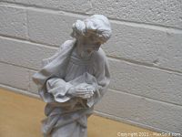 Front view of white porcelain figurine showing the man holding a lamb, displaying detailed facial features and clothing texture.