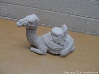 White porcelain camel figurine sitting, approximately 7 inches tall, showing side view with detailed saddle and harness.
