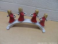 Set of four Goebel angel figurines holding candle holders on a curved silver-toned base against a plain wall background.