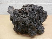 Front and side view of a large, dark lava rock with porous texture.