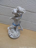 Full view of Algora porcelain cherub figurine showing front and left side with wings, horn of plenty, and blue sash