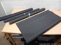 Four large rolls of black shade screen fabric on a table, one partially unrolled.