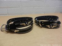 Photo showing pair of men's black leather belts coiled with stud and metal eagle decorations visible.