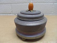 Side angled photo of the vintage music box showing wooden top with brown knob and metal base with three feet.