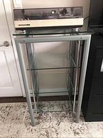 Full view of metal and glass stereo shelf with turntable on top, showing all glass shelves and metal frame.