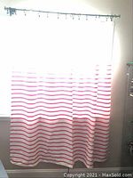 Shower curtain fully hanging on rod showing pink horizontal stripes over white fabric in a bathroom window area.