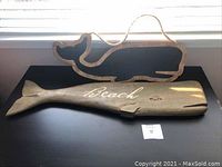 Both wooden whale decor pieces shown on black surface by a window with natural light.