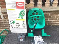 Green plastic child bike carrier seat with footrests, mounting hardware, instruction manual and original box shown on a surface in front of a brick wall.