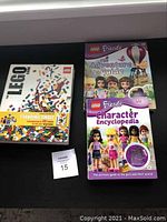 Three Lego books shown on black surface, The Lego Book with yellow band and minifigure, Lego Friends Adventure Guide, and Character Encyclopedia