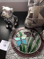 Photo of a silver-tone ceramic bulldog figurine, geometric pillow, and stained glass panel with butterfly and flower motif.