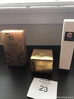 Three Elizabeth Grant Biocollasis Complex skincare products on a black surface next to a MaxSold auction tag number 23.