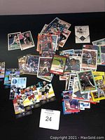Wide view of a selection of baseball and hockey cards spread on a black surface with lot number card in foreground.